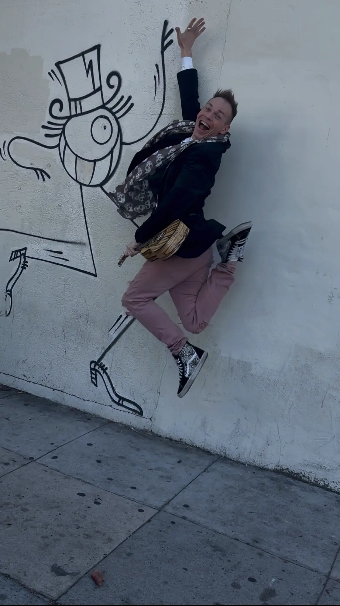 Ryan mid-jump against a white wall, high-fiving a cartoon figure in a top hat painted on the bricks